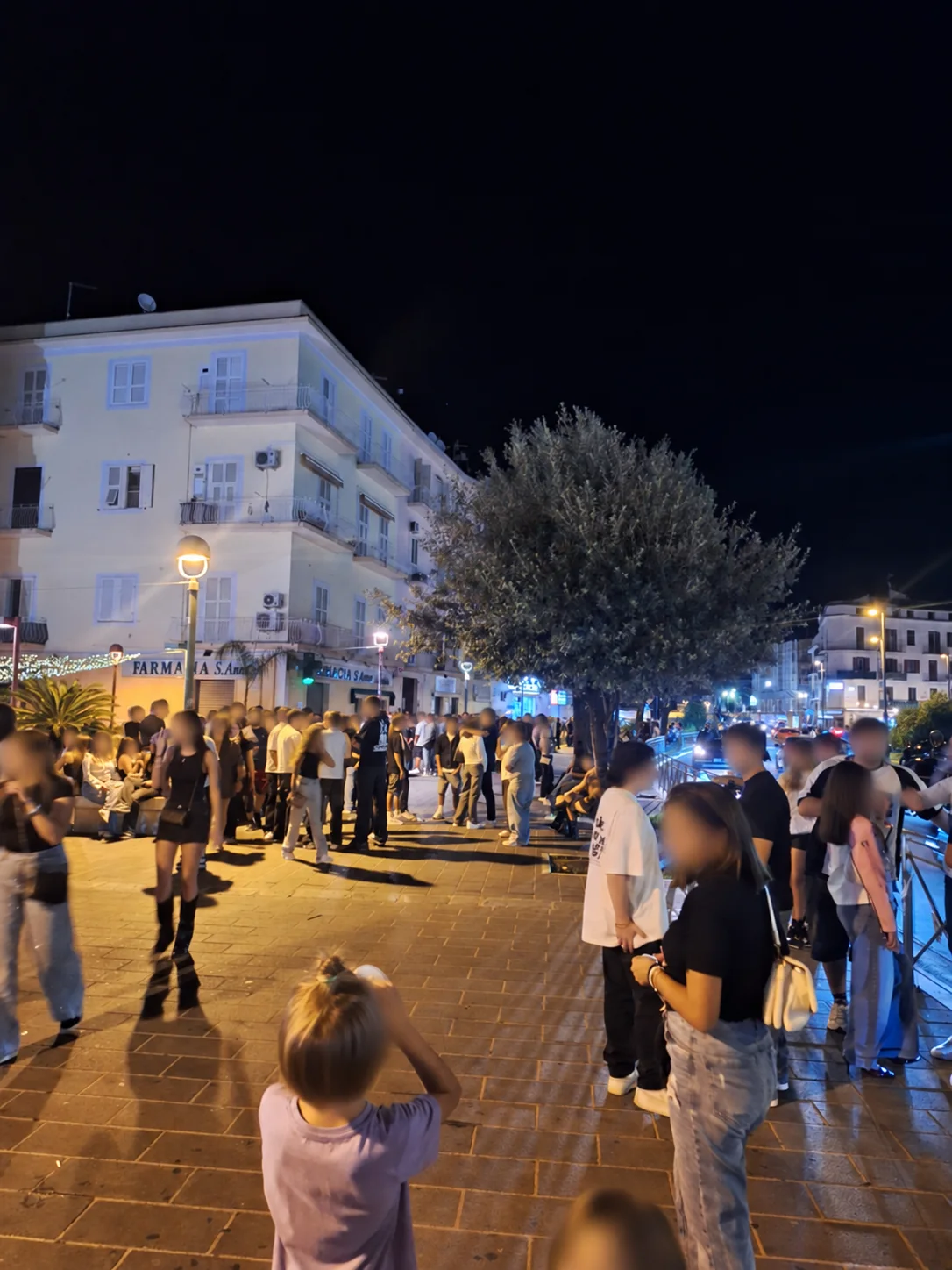 Gruppi di persone lungo la prima parte di Via Vitruvio durante il sabato sera