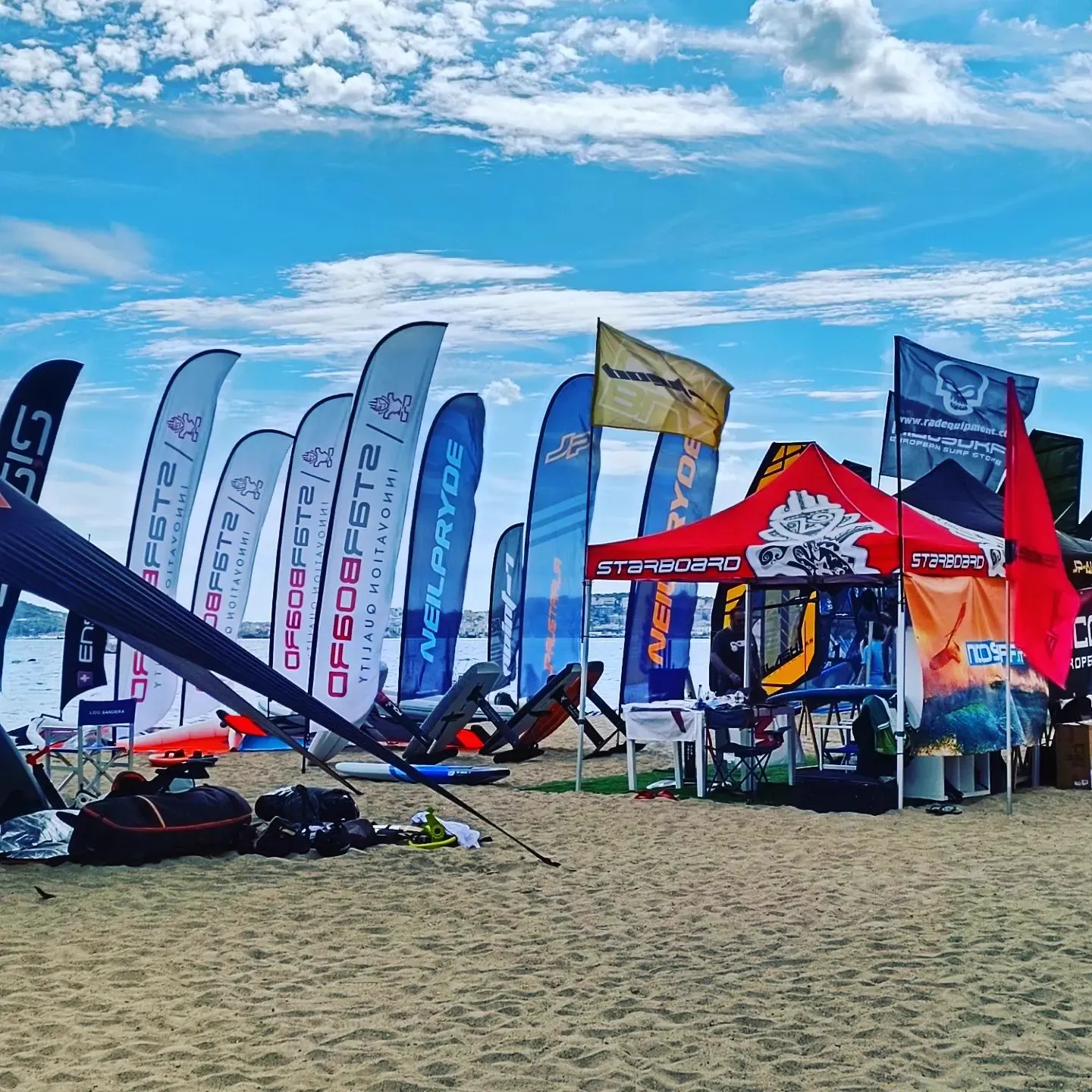 Tavole, vele e gazebo di una manifestazione di sport acquatici sulla spiaggia di Vindicio