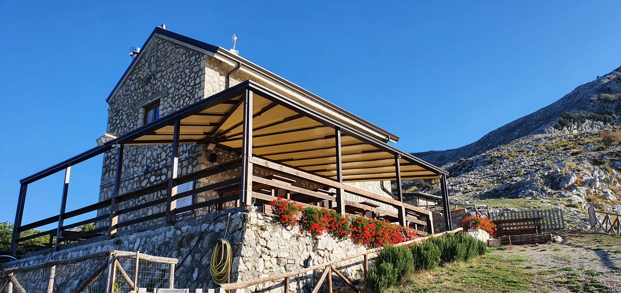 Il Rifugio di Pornito in pietra con la veranda coperta e il versante roccioso dei Monti Aurunci alle spalle